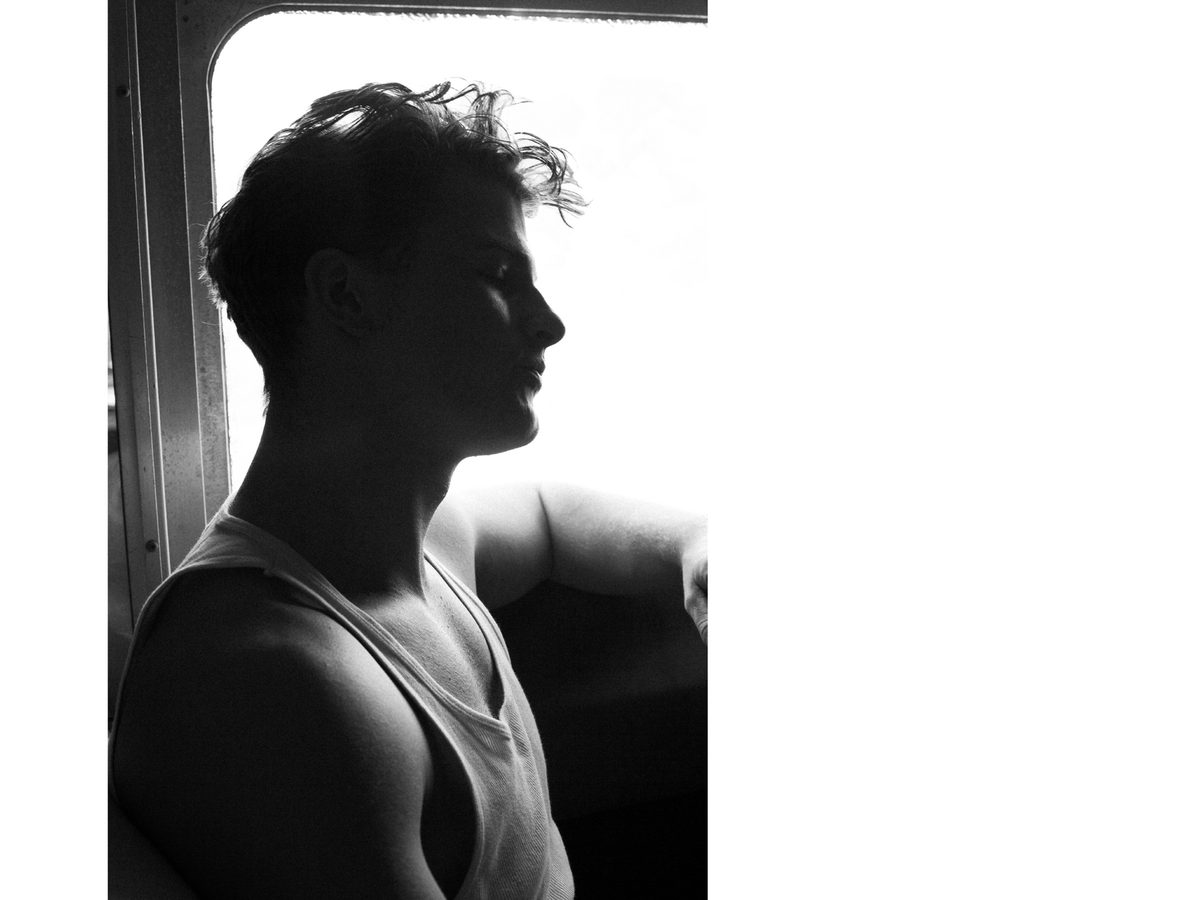 Spread 5 of 12 from On The Road: a young man in a tank top sits in silhouette and profile against a bright window; black and white.