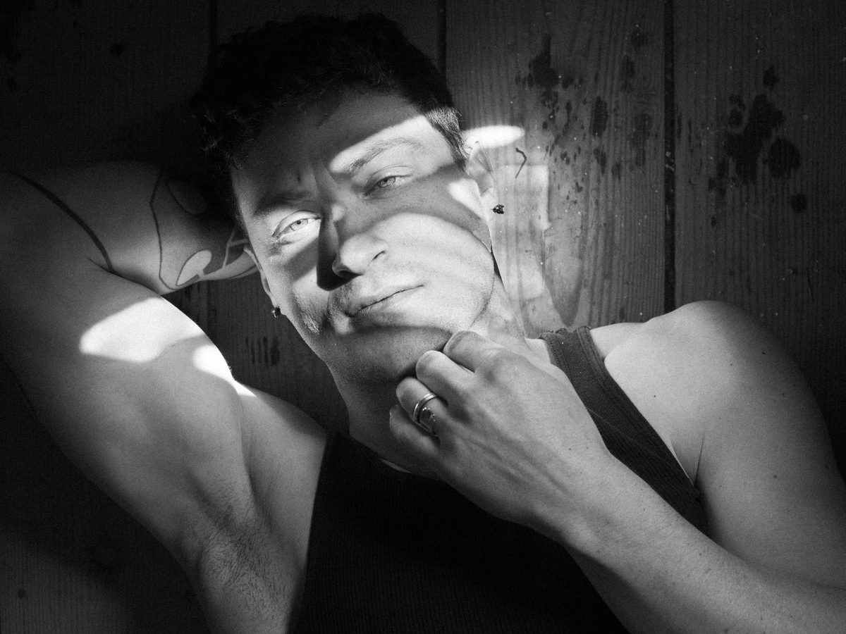 Spread 1 of 6 from Ashland: a close portrait of a man in a tank top, light falling across his face, hand at his jaw; black and white.