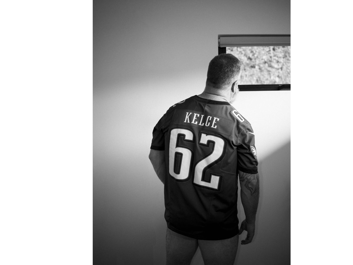 Spread 1 of 10: a man in a sports jersey stands at a window, seen from behind; black and white.