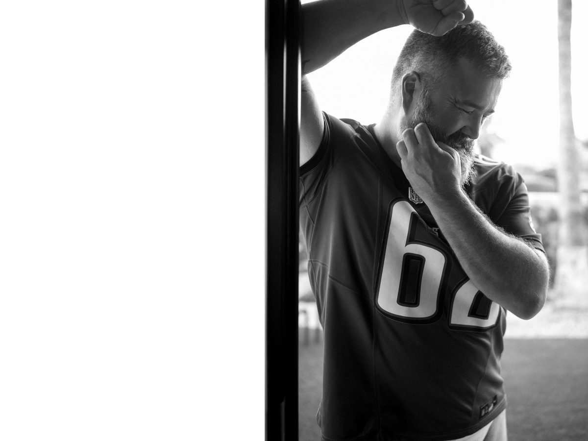 Spread 2 of 10: a bearded man in a sports jersey leans against a post outdoors, hand at his chin; black and white.