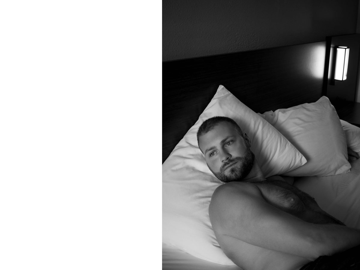 Spread 1 of 11 from Motel 6: a bearded man lies on a motel bed pillow, looking at the camera; black and white.